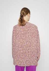 Blouse ample à motif coloré à pois avec des teintes d'orange, de violet et de beige. Manches longues et col arrondi.