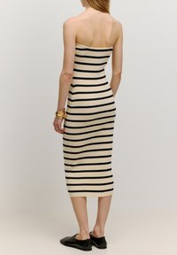 Gestreepte bodycon jurk in crème en zwart, ribbelstructuur, strapless ontwerp, knielang, gecombineerd met zwarte platte schoenen.