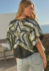 Crni i dušičasti top sa šljokicama u zvjezdastom uzorku, labavog kroja i kratkim rukavima, u kombinaciji sa svijetloplavim trapericama.