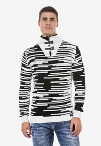 Gestreifter Pullover aus Strick in Schwarz und Weiß mit hohem Kragen, der einen Reißverschluss und Knopfakzente aufweist, strukturiertes Rippendesign und taillierte Ärmel.
