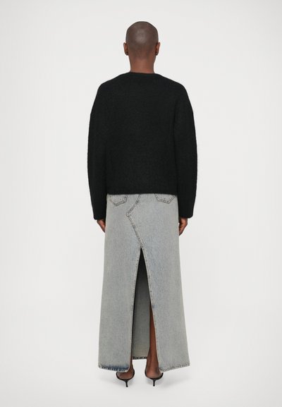 Suéter preto de malha com mangas largas, combinado com uma saia longa de denim cinza com uma fenda até a coxa e detalhes de costura únicos.