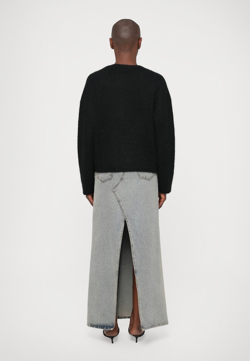 Maglione nero lavorato a maglia con maniche larghe, abbinato a una lunga gonna in denim grigia con uno spacco alto alla coscia e dettagli di cucitura unici.