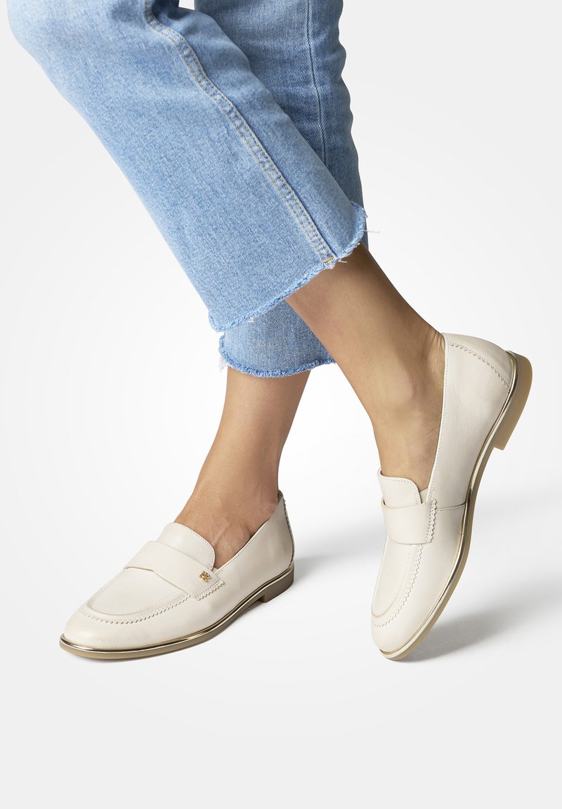 Beige leren loafers met een verhoogde naad, een platte hiel met een gouden accent en een brede band over de bovenkant. Gecombineerd met cropped denim jeans.