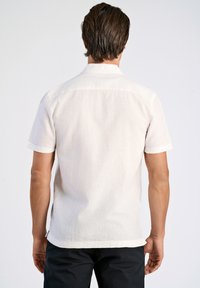 Camicia a maniche corte in tessuto beige chiaro, con colletto standard e maniche arrotolate, orlo dritto e texture sottile.