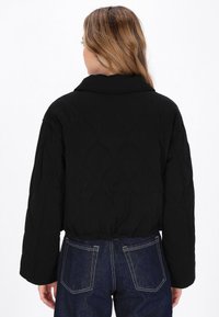 Zwarte gewatteerde jas met een cropped ontwerp, voorzien van een brede kraag en lange mouwen, gecombineerd met donkerblauwe spijkerbroeken.