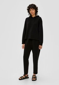 Zwarte hoodie met een ontspannen pasvorm, gecombineerd met tapered zwarte broeken en zwarte sandalen met bandjes. Soepele stof, minimalistisch ontwerp.