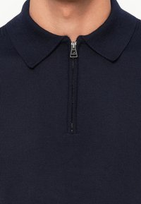 Camiseta polo azul marino con una cremallera corta, textura acanalada y un diseño de cuello clásico. Presenta un estilo minimalista sin patrones.