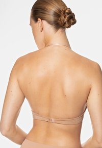 Achteraanzicht van een naakt beha met zachte stof, verstelbare banden en een haaksluiting. Soepele textuur met minimale zichtbare hardware.