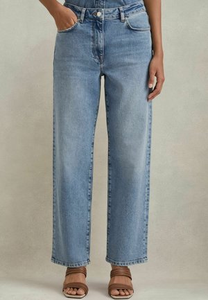 Jeans de pierna ancha de color azul claro, fabricados en denim, con una cintura alta, bolsillos frontales y un dobladillo limpio. Combinados con sandalias de tiras marrones.