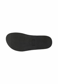 Semelle de chaussure en caoutchouc noir avec motif de grip en chevron et étiquette de marque rectangulaire au centre sur fond blanc.