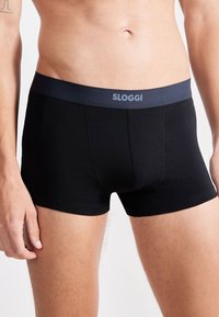 Musta puuvillainen bokserit, joissa on tumma vyötärö, jossa lukee "SLOGGI" vaaleansinisellä. Kangas on sileä ja tiukka istuvuus.