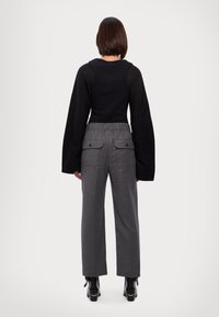Haut noir à manches longues avec un corsage ajusté ; pantalon large gris avec taille élastique et poches arrière ; bottes à talons noires.