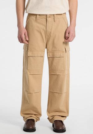 Beige cargobroek met een losse pasvorm, voorzien van meerdere voorzakken, riemlussen en een opgerolde zoom. Gemaakt van duurzaam katoen.
