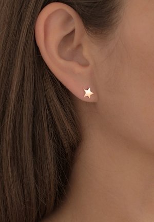 Sternförmiger Ohrstecker aus Roségold, der am Ohr präsentiert wird. Glatte Oberfläche, minimalistisches Design, das die natürliche Form des Ohrläppchens betont.