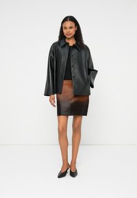 Casaco de couro preto com punhos oversized, cinco botões, combinado com uma saia de couro castanha com textura degradê. Sapatilhas pretas de bico fino.