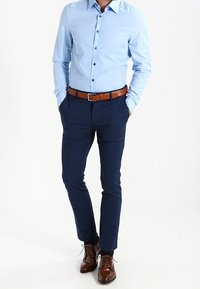 Ljusblå skjorta med knappar i mörk färg, marinblå smalpassande byxor, brun läderbälte och bruna slipskor. Slät textur, skräddarsydd passform.