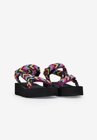 Sandalias coloridas con una correa tejida y estampada en diseño de zigzag en rosa, verde y amarillo, montadas sobre una suela de plataforma negra gruesa.