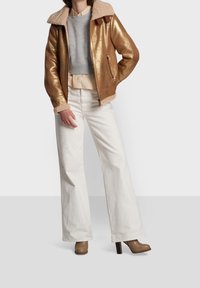 Metallic gold bomber jacket with a faux shearling collar, paired with a grey cropped sweatshirt, white wide-leg jeans, and brown heeled boots.