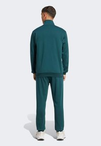 Survêtement turquoise avec col montant et fermeture éclair, texture lisse, manches longues et pantalons assortis avec une coupe décontractée.