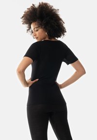 Zwart T-shirt met korte mouwen, met een aangesloten ontwerp en een zachte textuur. Geprobeerd door een model met krullend haar, gecombineerd met vergelijkbare zwarte leggings.