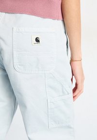 Light blue cargo pants with multiple pockets, featuring a square patch logo. Soft cotton material with a relaxed fit.