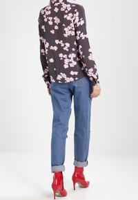 Blouse fleurie foncée avec des fleurs roses, associée à un jean en denim retroussé et des bottes rouges à talons hauts. Texture lisse ; coupe décontractée.