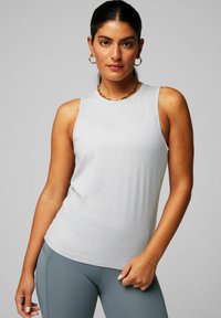 Helles graues ärmelloses Tank-Top aus glattem Stoff, mit einem runden Halsausschnitt und einer taillierten Silhouette. Kombiniert mit grauen Leggings.