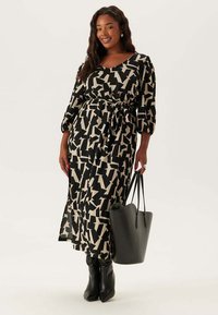 Abito a motivi neri e crema con maniche a sbuffo lunghe, vita cinchita e una spaccatura, abbinato a una borsa a mano grigia e stivali neri fino al ginocchio.