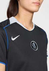 Svart sportsdrakt med korte ermer, med en lys blå krage, blå detaljer, Nike-logo, og et rundt lagmerke med en løve.
