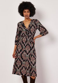 Czarna sukienka o kroju kopertowym, zdobiona kwiatowym wzorem paisley w odcieniach czerwieni i kremu, z rękawami o długości trzy czwarte i rozkloszowanym dołem. Miękka tekstura materiału.