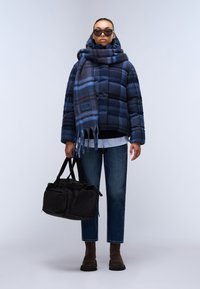 Quiltet marineblå ternet pufferjakke med hætte, parret med et blått og gråt stribet tørklæde. Casual blå jeans og sort fodtøj fuldender looket.