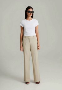 White short-sleeve t-shirt paired with beige tailored pants. Black sunglasses complete the outfit, emphasizing a sleek, modern look.