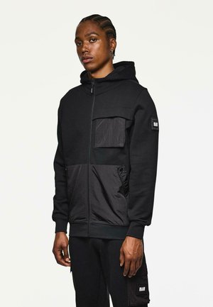 Zwarte rits hoodie met een mix van textuurstoffen, een grote voorkantzak en ribgebreide manchetten. Verfraaid met een merkembleem op de borst.
