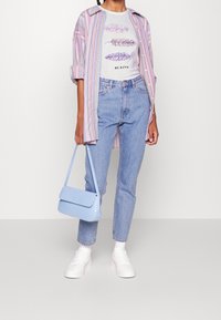 Camisa de rayas oversized, camiseta gráfica blanca con plumas, jeans azul claro con detalles sutiles, zapatillas blancas y un bolso azul claro.