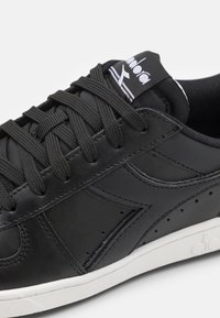 Black leather sneaker with textured surface, matching laces, white outsole, and logo on tongue. Features perforated accents on sides.