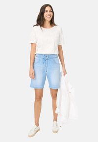 Shorts en denim bleu clair avec une taille à nouer et des ourlets roulés, associés à un t-shirt blanc à texture florale et des baskets blanches.