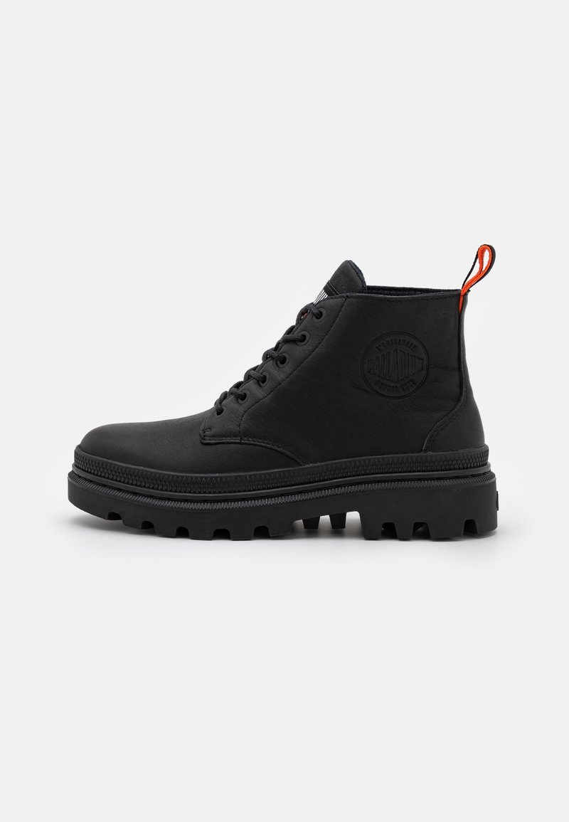Botte mi-hauteur en cuir noir avec semelle épaisse à crampons, fermeture à lacets à l'avant, logo embossé sur le côté et languette orange au talon sur fond blanc.