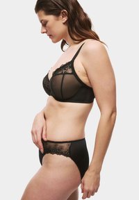 Zwart lingeriesetje bestaande uit een doorschijnende beha met bloemenkantaccenten en bijpassende slip met een geborduurd bloemenpatroon, beide met een gegolfde rand.