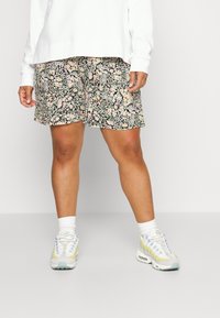 Shorts fleuris noirs avec des motifs roses et blancs ; matière légère ; longueur au-dessus du genou ; assortis à des baskets blanches et des chaussettes mi-mollet.