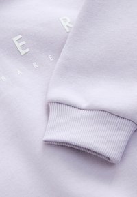 Felpa lilla con polsini a costine e testo bianco in rilievo. Tessuto morbido con una texture liscia e un fit rilassato.