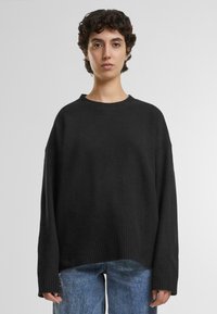 Schwarzer, übergroßer Pullover mit geripptem Saum und Bündchen, aus weichem Material; hat einen runden Halsausschnitt und weiter fallende Schultern.
