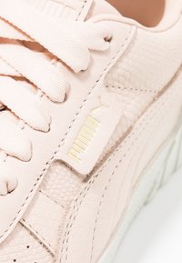 Baskets Puma en cuir rose doux avec un design texturé, logo doré et lacets assortis, dotées d'une semelle en caoutchouc blanche.