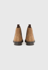 Botas de tobillo de ante marrón con paneles laterales elásticos, tiradores y suelas de goma negra. Textura suave con un diseño elegante y minimalista.