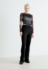 Pantalons longs noirs associés à un haut transparent à manches longues à motifs présentant un dégradé de tons de gris et un design tordu.