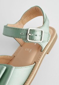 Lysegrøn sandal med justerbar rem med sølvspænde og beige polstret sål, størrelse UK 6 synlig på indersålen.