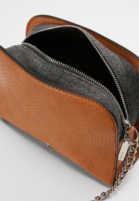 Brun faux slangeskind håndtaske med interiør af gråt filt, sølv lynlås og kæderek. Tasken er semi-struktureret med afrundede kanter.