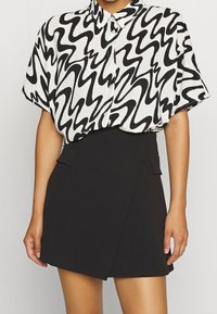 Černobílá košile s abstraktním potiskem, krátkými rukávy a límečkem, doplněná černou zavinovací sukní s bočními kapsami.