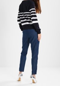Pull en maille rayé bleu marine et blanc, assorti à un pantalon slim bleu foncé et des chaussures à talons hauts argentées, vu de dos.