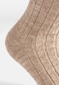 Calza di lana beige lavorata a maglia con un motivo a trama, caratterizzata da coste e una finitura liscia. Il materiale appare morbido e caldo.