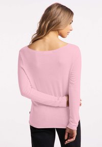 Lange mouw roze top met een brede halslijn en een soepele textuur. De achterkant is rond en de mouwen zijn aansluitend met minimale ontwerpelementen.